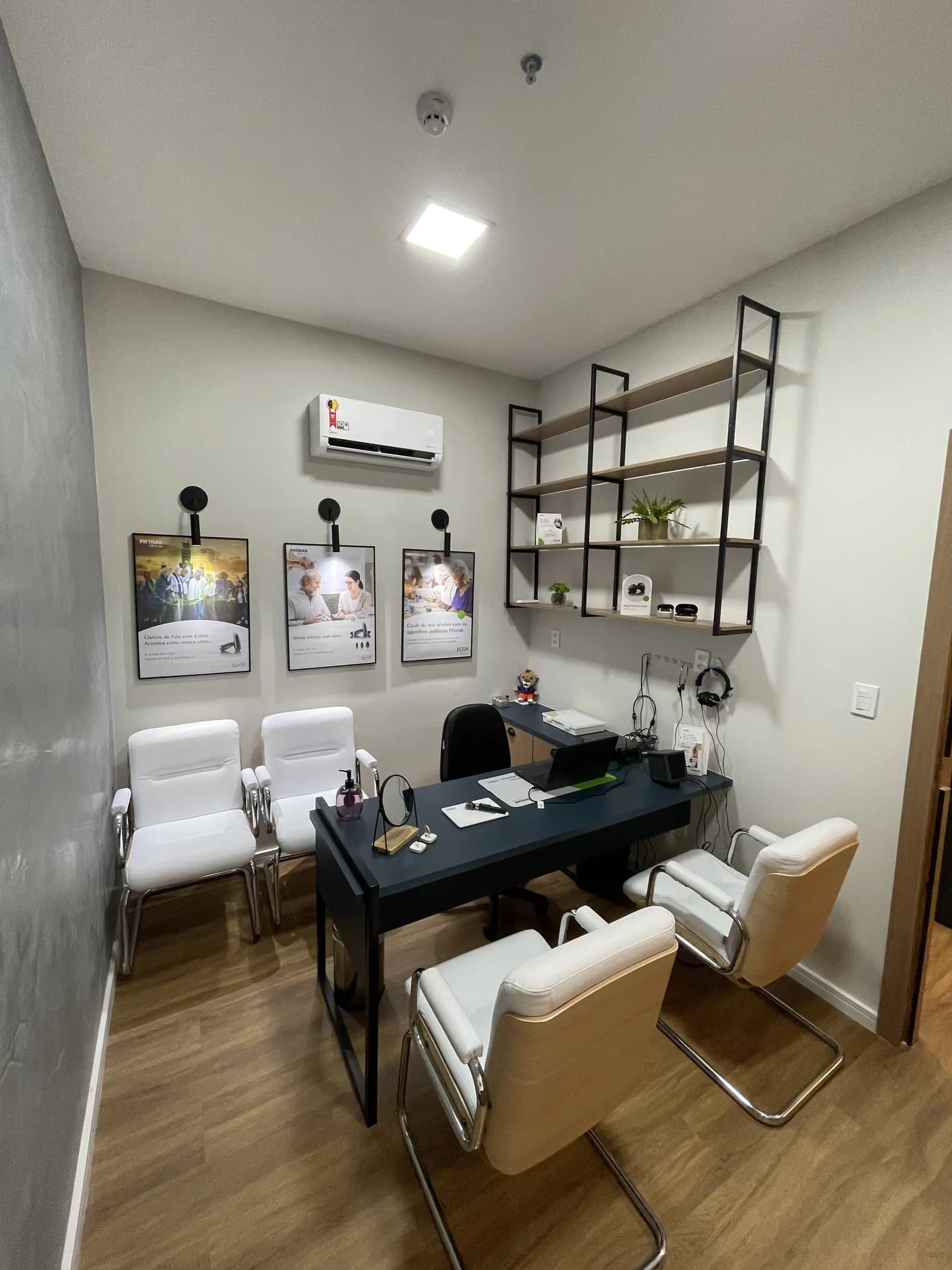 Sala de atendimento da Audion, com mesa de consulta e pôsteres Phonak na parede