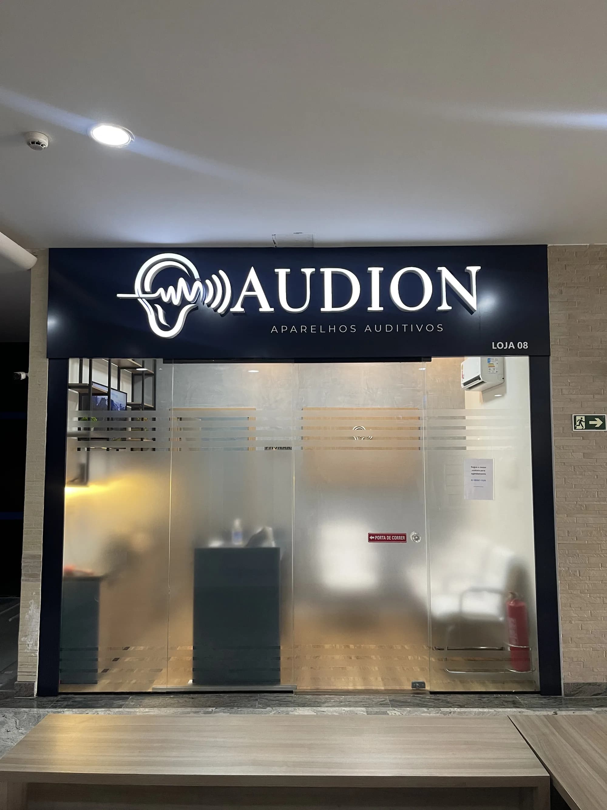 Fachada da Audion, na Harmony Jatiúca, em Maceió, com a fachada iluminada e porta de vidro de entrada